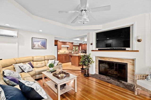 living area with a ceiling fan, light wood-style flooring, a fireplace with flush hearth, a wall mounted air conditioner, and recessed lighting