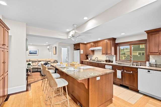 kitchen with under cabinet range hood, white appliances, a kitchen island, a kitchen breakfast bar, and open floor plan