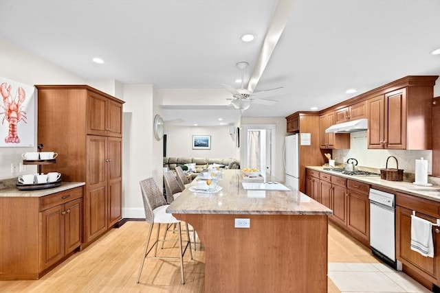 kitchen with a breakfast bar, freestanding refrigerator, a kitchen island, ceiling fan, and under cabinet range hood