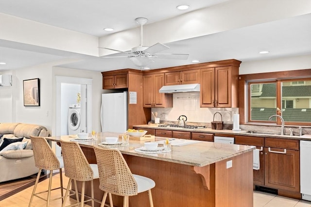 kitchen with freestanding refrigerator, a sink, light stone countertops, under cabinet range hood, and dishwashing machine