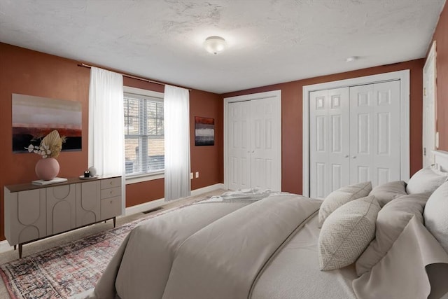 bedroom with baseboards, visible vents, and two closets