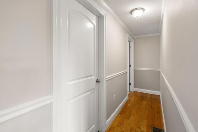 hall with light wood-type flooring, baseboards, visible vents, and crown molding