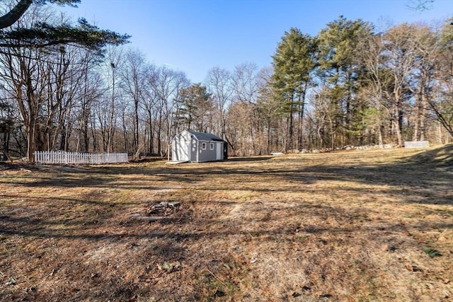 view of yard featuring a storage shed, fence, an outdoor structure, and a view of trees