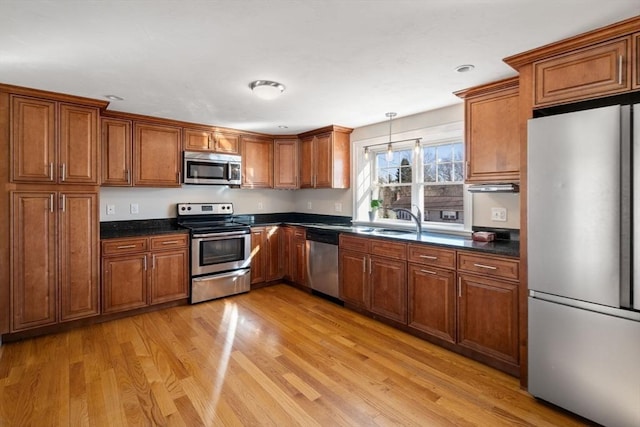 kitchen featuring pendant lighting, light wood-type flooring, brown cabinets, and appliances with stainless steel finishes