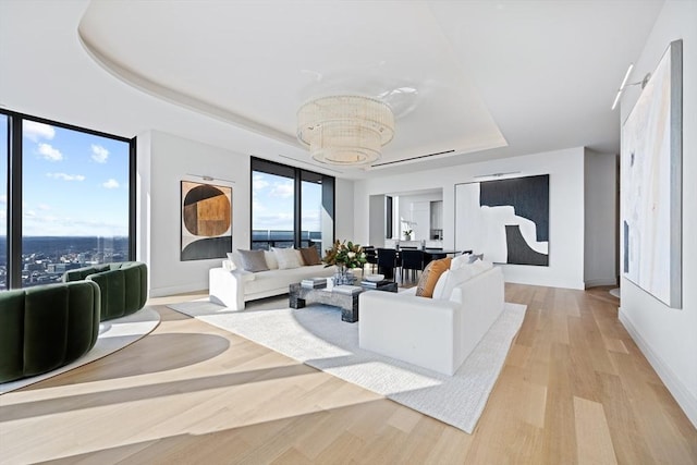 living room featuring a wealth of natural light, a tray ceiling, light hardwood / wood-style flooring, and a notable chandelier