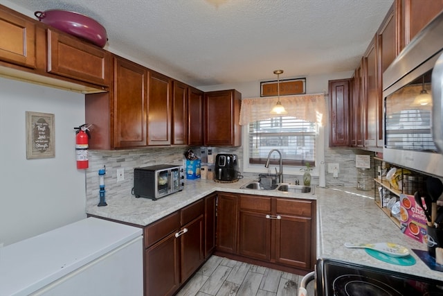 kitchen featuring stove, decorative backsplash, sink, white fridge, and pendant lighting