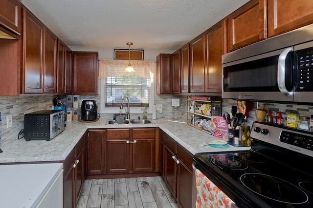 kitchen with hanging light fixtures, sink, backsplash, stainless steel appliances, and light hardwood / wood-style floors