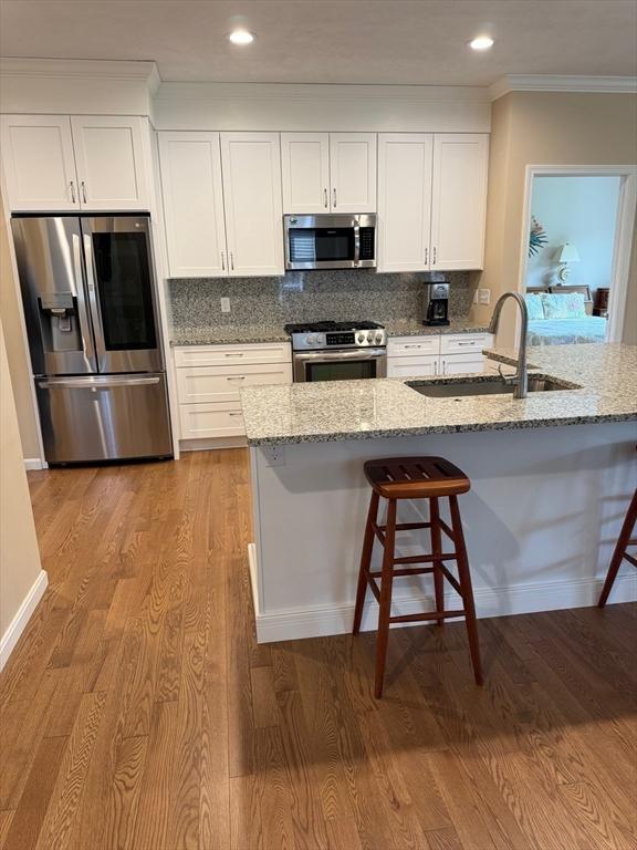 186 Stone Hill Dr Unit 186, Northbridge, MA 01588 - kitchen featuring appliances with stainless steel finishes, a sink, light stone countertops, light wood-style floors, and ornamental molding