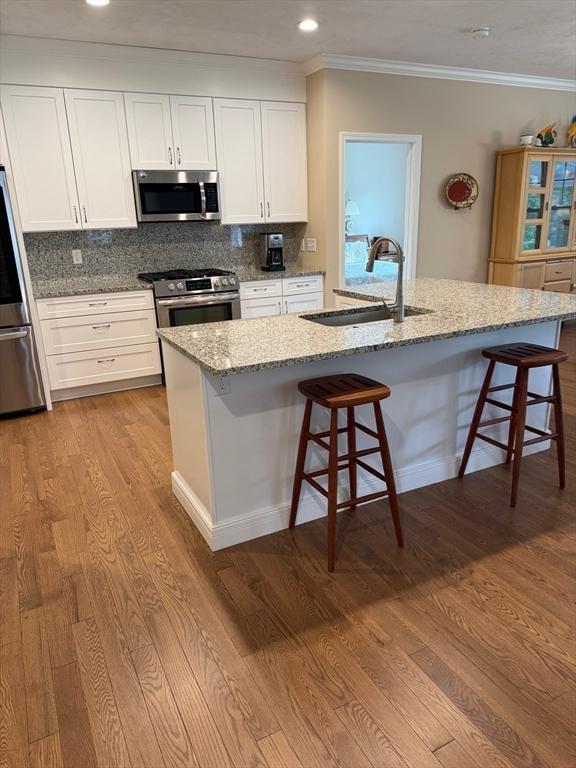 186 Stone Hill Dr Unit 186, Northbridge, MA 01588 - kitchen with stainless steel appliances, a sink, wood finished floors, a kitchen bar, and light stone counters