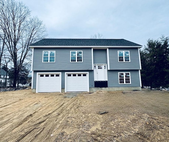 split foyer home with an attached garage, a shingled roof, and dirt driveway