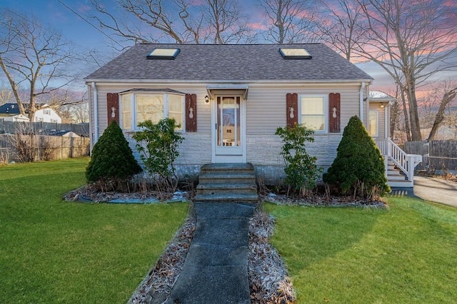 view of front of home featuring stone siding, roof with shingles, a front lawn, and fence