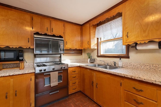 kitchen featuring range with gas cooktop, black microwave, light countertops, brown cabinets, and a sink