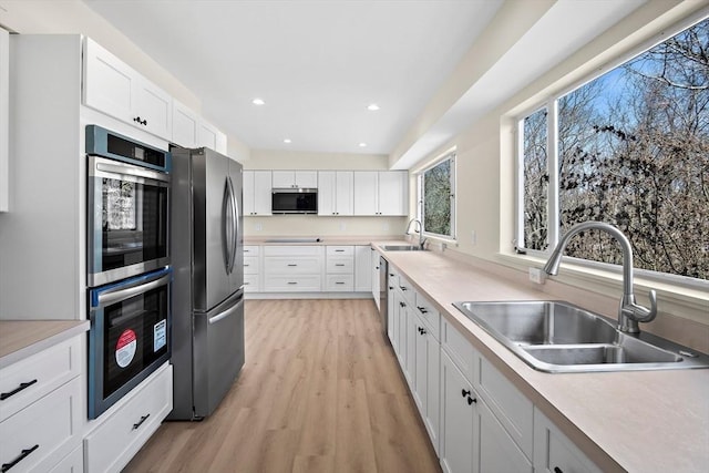 kitchen with appliances with stainless steel finishes, a sink, light wood-type flooring, white cabinetry, and recessed lighting