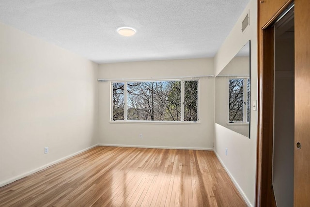 empty room with light wood-type flooring, healthy amount of natural light, baseboards, and a textured ceiling