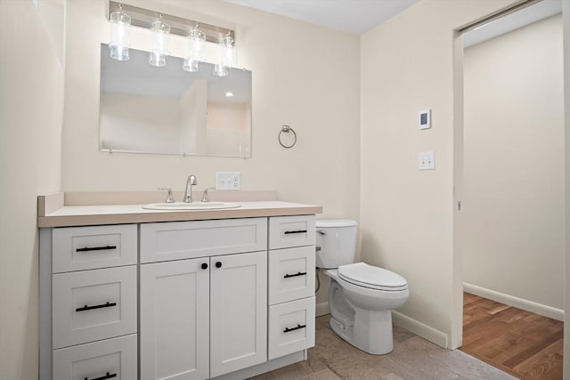 bathroom featuring toilet, vanity, baseboards, and wood finished floors