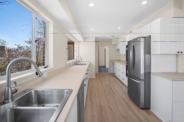 kitchen featuring appliances with stainless steel finishes, a sink, light wood-type flooring, white cabinetry, and recessed lighting