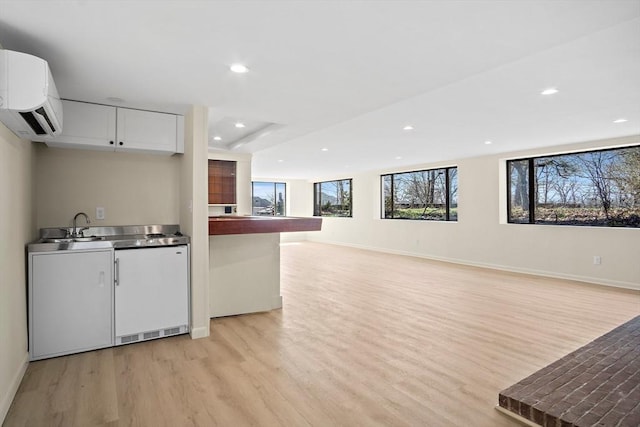 kitchen with light wood finished floors, an AC wall unit, baseboards, a sink, and recessed lighting