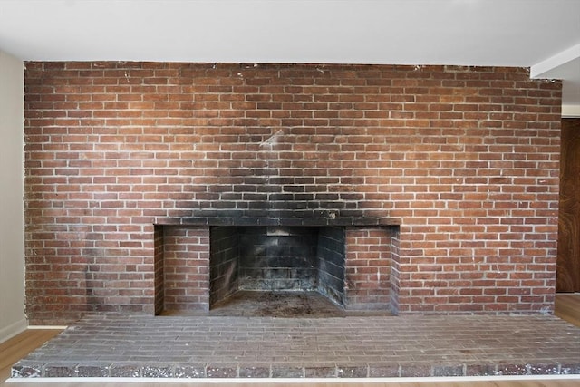 detailed view of a brick fireplace, wood finished floors, and baseboards