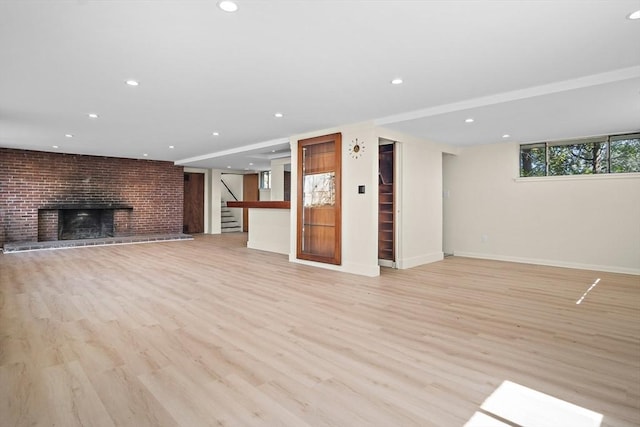 below grade area with light wood finished floors, a brick fireplace, recessed lighting, stairs, and baseboards