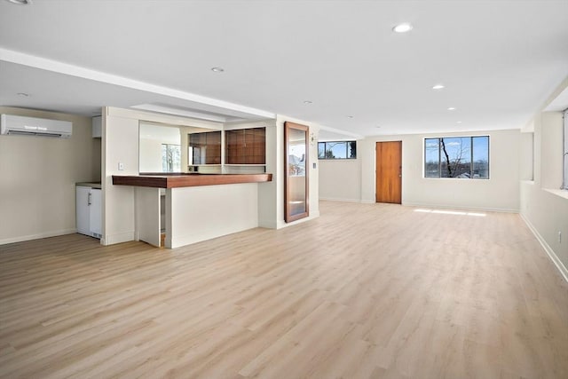 unfurnished living room featuring a wall unit AC, light wood finished floors, recessed lighting, and baseboards