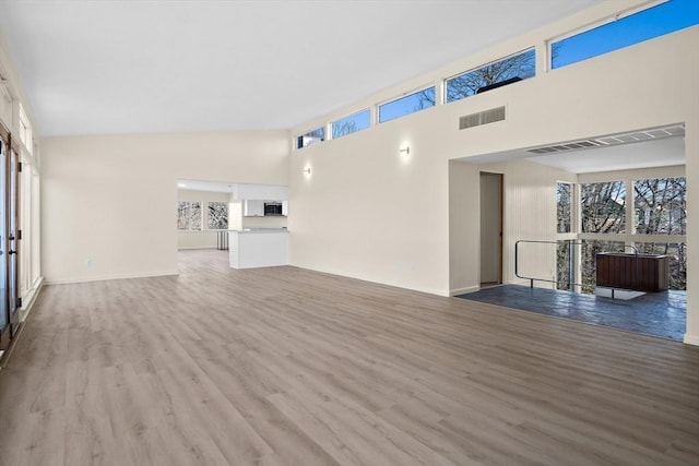 unfurnished living room with wood finished floors, plenty of natural light, and a high ceiling