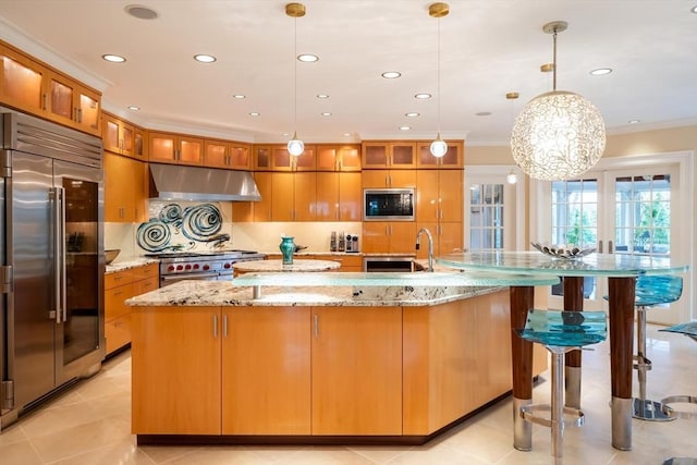 kitchen with a large island, built in appliances, light stone countertops, sink, and decorative light fixtures