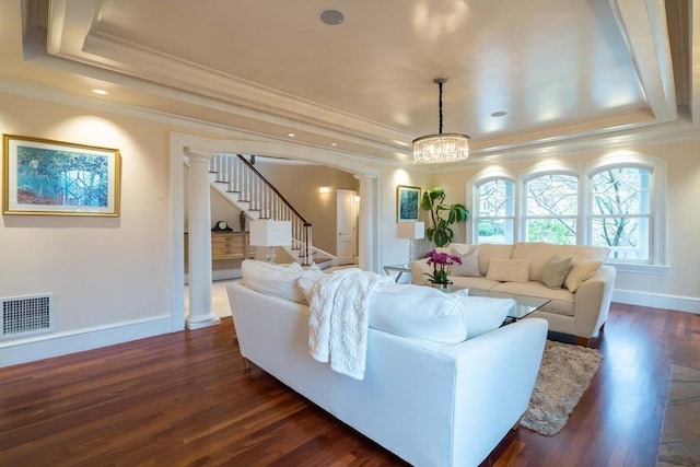 living room featuring a chandelier, crown molding, dark hardwood / wood-style flooring, a tray ceiling, and decorative columns