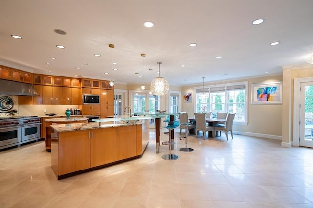 kitchen featuring hanging light fixtures, black microwave, light stone countertops, range with two ovens, and a spacious island