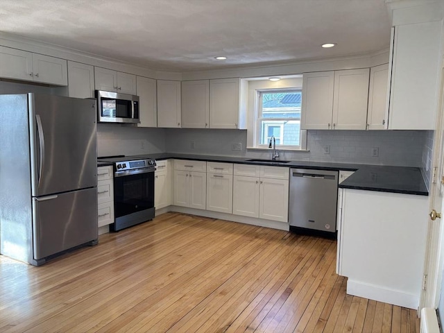 kitchen featuring stainless steel appliances, dark countertops, decorative backsplash, a sink, and light wood-type flooring