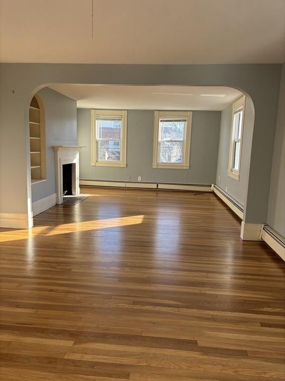 unfurnished living room with a baseboard heating unit, a fireplace, wood finished floors, built in features, and baseboard heating