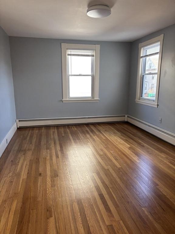 spare room featuring a baseboard heating unit, dark wood finished floors, and baseboards