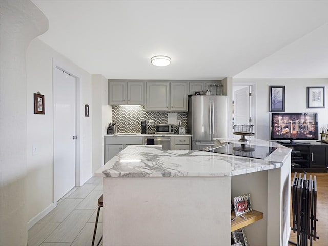 kitchen featuring stainless steel appliances, a center island, gray cabinets, and a kitchen bar