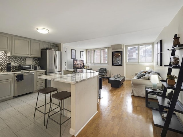 kitchen featuring gray cabinets, a breakfast bar area, a center island, light stone counters, and stainless steel appliances