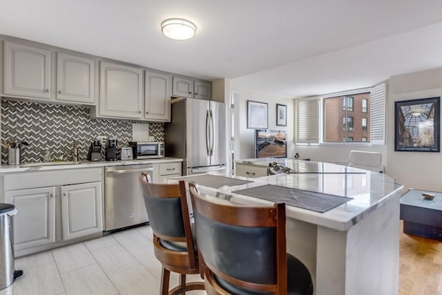 kitchen featuring backsplash, gray cabinets, stainless steel appliances, and a center island