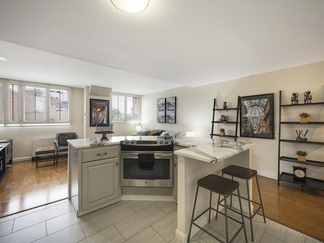 kitchen featuring light stone counters, light hardwood / wood-style flooring, electric range, a kitchen breakfast bar, and a kitchen island