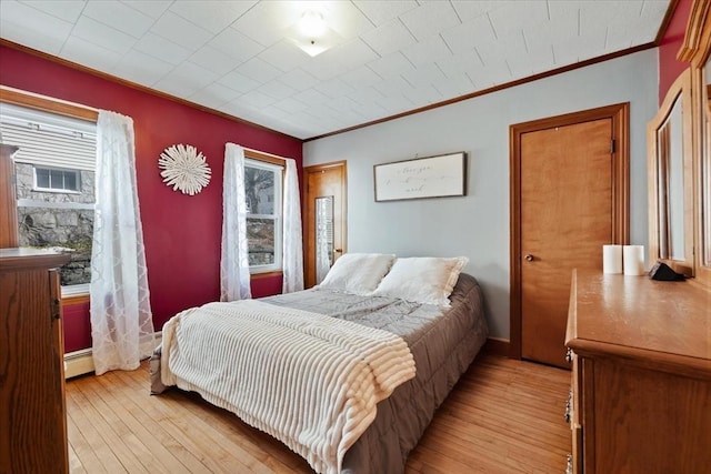 bedroom with baseboard heating, crown molding, and light wood finished floors