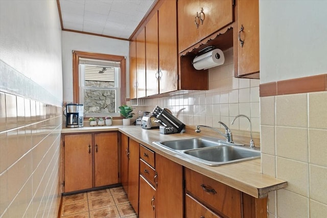 kitchen featuring light tile patterned floors, ornamental molding, brown cabinets, light countertops, and a sink