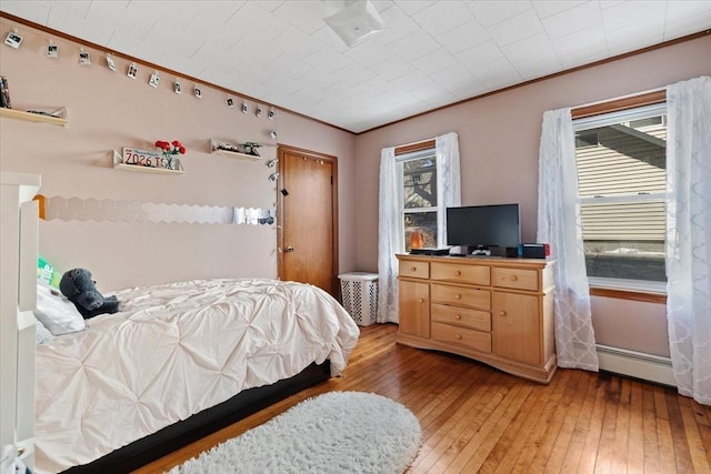 bedroom with ornamental molding, light wood-type flooring, and baseboard heating