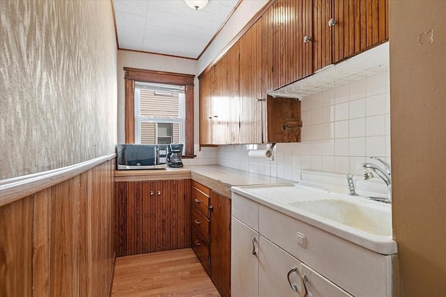 kitchen with light wood-style floors, light countertops, decorative backsplash, brown cabinetry, and crown molding