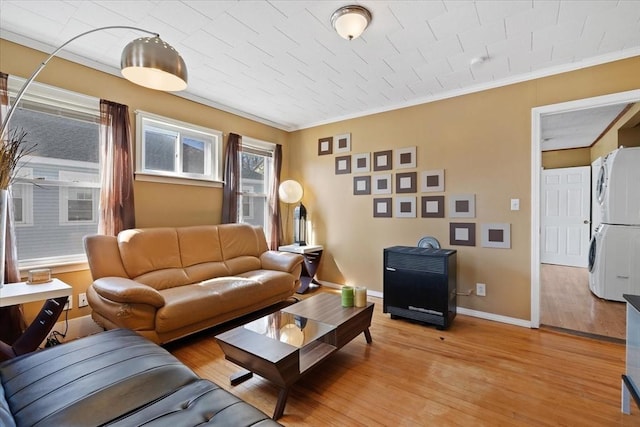 living room with stacked washer and dryer, ornamental molding, light wood-style flooring, and baseboards