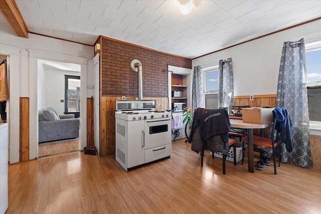 kitchen featuring white gas range oven, light wood-type flooring, ornamental molding, and plenty of natural light