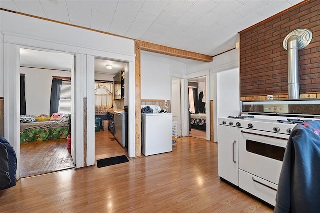 kitchen with light wood-type flooring, white gas range oven, washing machine and dryer, and white cabinetry