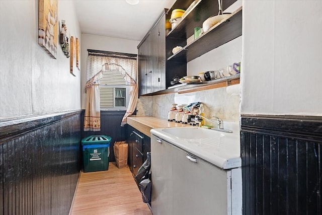 kitchen with a wainscoted wall, light countertops, light wood-type flooring, open shelves, and a sink