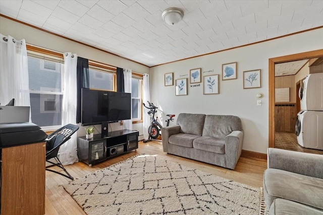 living area featuring crown molding, baseboards, stacked washer and clothes dryer, and light wood-style floors