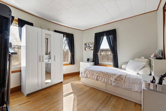 bedroom featuring light wood finished floors, baseboards, and crown molding