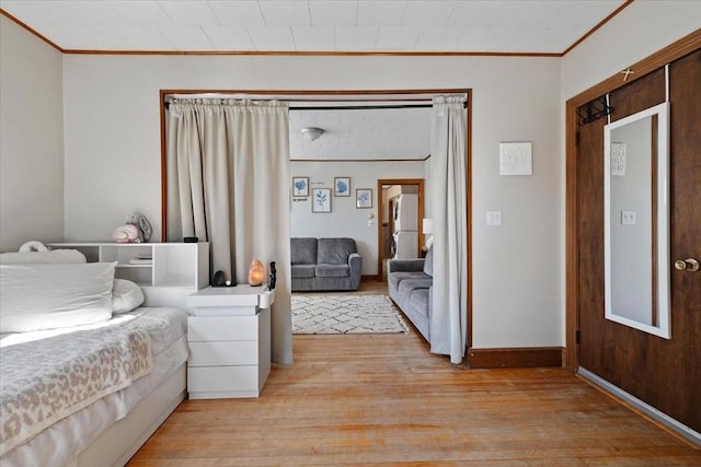 bedroom with light wood-style floors, freestanding refrigerator, and crown molding