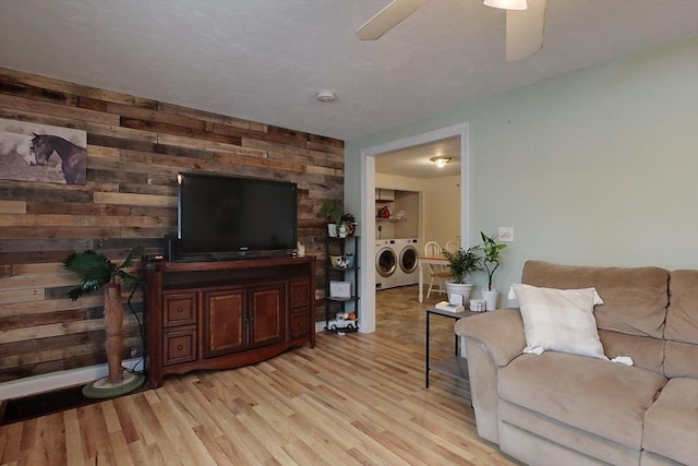 living room with ceiling fan, washing machine and clothes dryer, light wood-type flooring, and wood walls