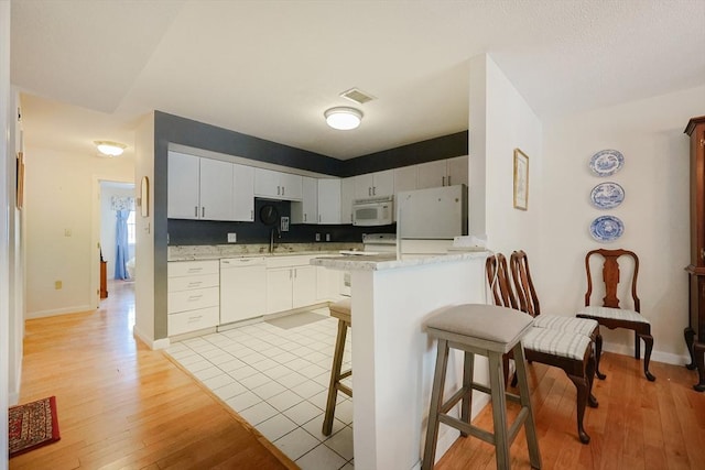 kitchen with white appliances, a kitchen breakfast bar, white cabinets, kitchen peninsula, and light wood-type flooring