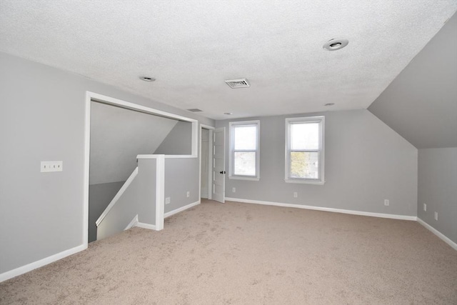 additional living space with a textured ceiling, carpet floors, vaulted ceiling, and visible vents