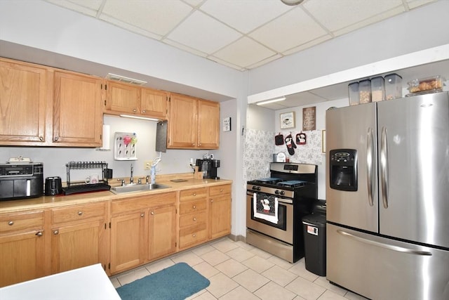 kitchen with light tile patterned floors, stainless steel appliances, a paneled ceiling, light countertops, and a sink